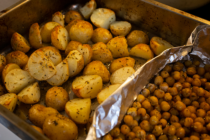 Potatis och kikärtor med en gyllenbrun yta som precis tagits ut från ugnen. Ovanpå finns lite kryddor. 
